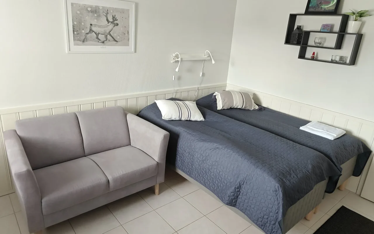 Grey sofa next to two single beds with navy covers in the 21 m² B apartment, Levi