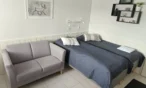 Grey sofa next to two single beds with navy covers in the 21 m² B apartment, Levi