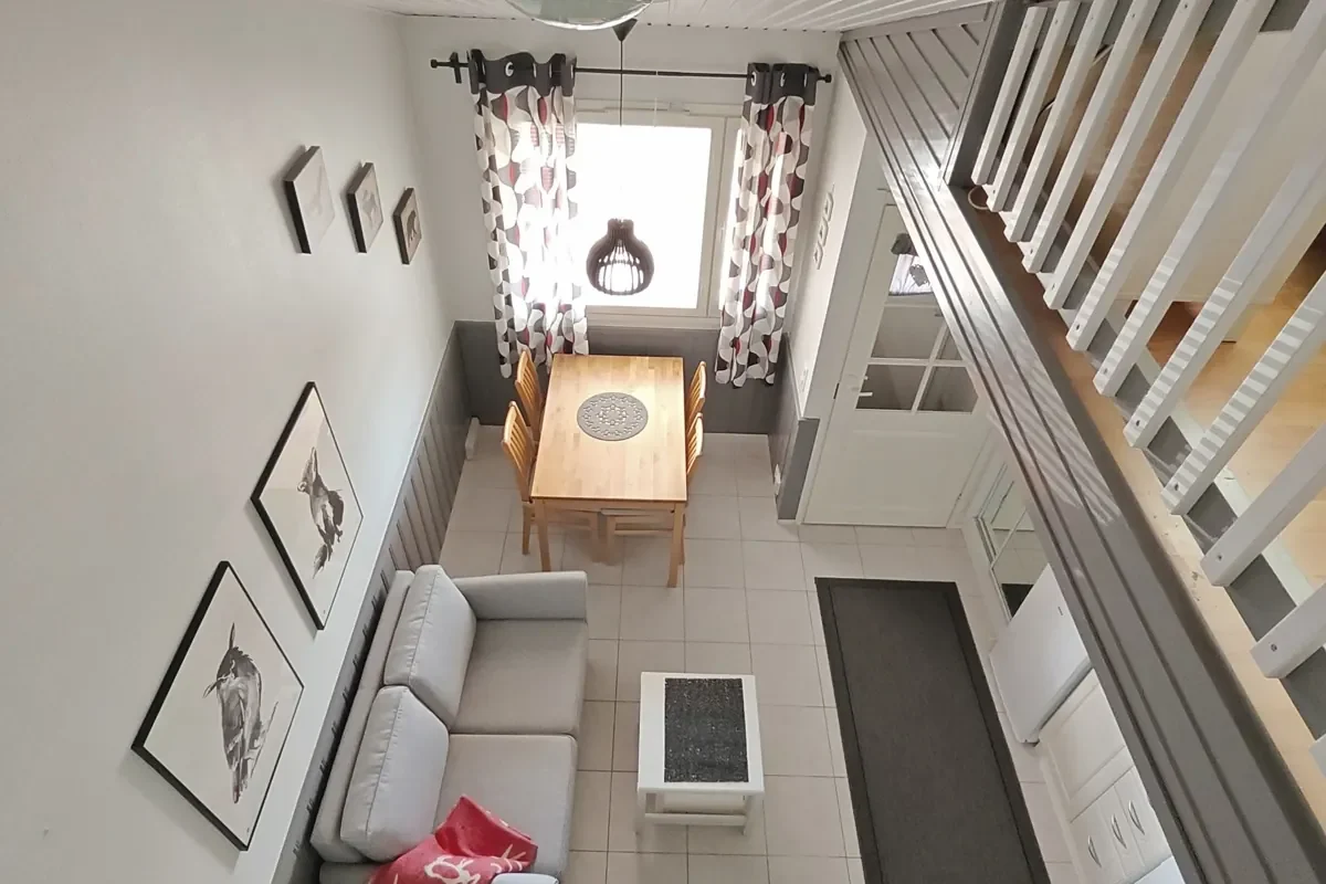 Dining table, sofa and kitchenette seen from the loft stairs in the 27 m² A apartment, portrait view